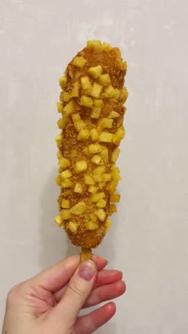 A sausage in a breaded crust made of dough and French fries on a stick. A human hand holds the trendy fast food