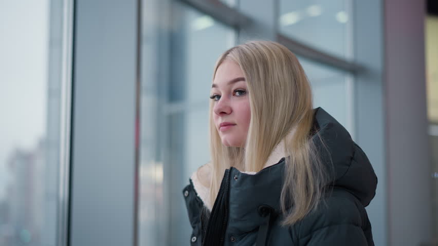 Lady with hair cascading down her shoulder, looking contemplative with urban background visible through glass window, a moment of serenity and reflection