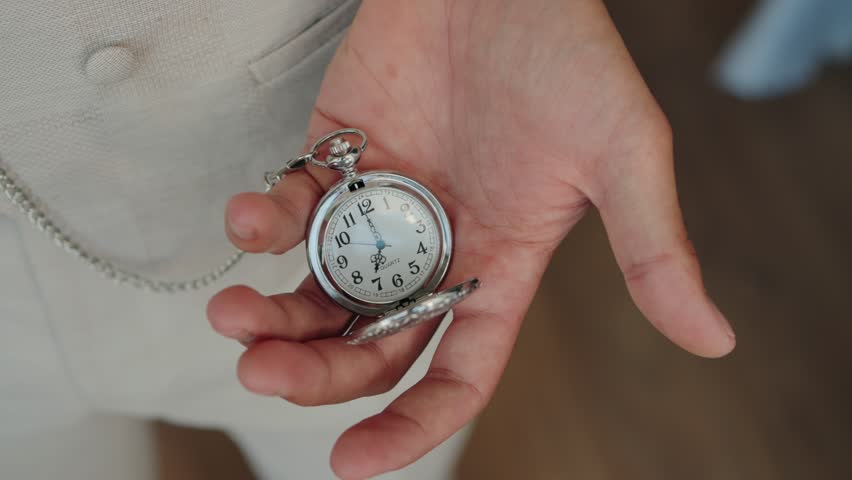 Close up of hand holding silver pocket watch with chain on soft daylight