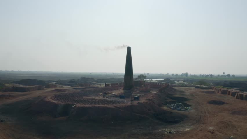Aerial shot of a chimney emitting smoke during daytime at a village near Sukkur Sindh, Pakistan.
