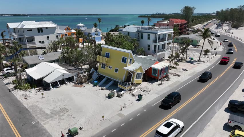 Hurricane Storm damage of yellow house in Bradenton Beach, Florida. Sunny day on Florida. Traffic on coastal road. Aerial rising wide shot.