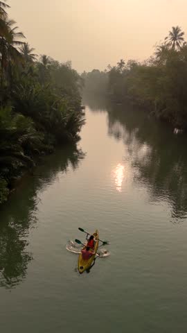 Early morning a couple paddling on tranquil waters in Chumphon Thailand reveals a stunning river scene. Silhouetted kayak glides alongside lush vegetation reflecting the soft light of dawn.