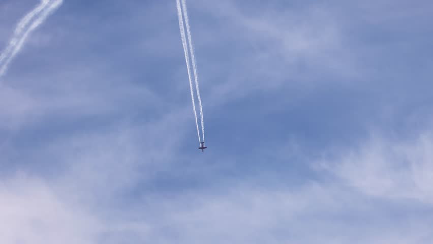 Two aircraft perform synchronized aerobatics against a clear blue sky, leaving white smoke trails during a 20-second airshow