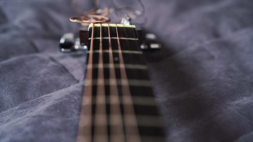 The camera flies smoothly from the upper fretboard to the guitar deck of a handcrafted spruce acoustic guitar, using a open aperture to create pronounced bokeh and blur that enhances the instrument