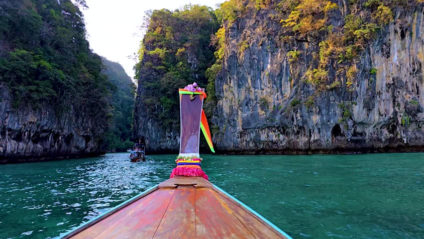 A long-tail boat navigates through emerald waters, surrounded by dramatic limestone cliffs adorned with lush greenery. Koh Hong Island Krabi