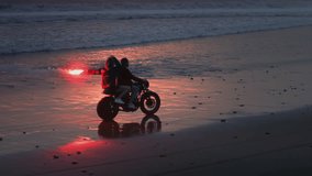 Couple rides a motorcycle on black tropical Bali beach. Girl holds a red warning light, man drives a motorcycle. Woman burns flame rescue torch, male controls a bike, sand. Ocean or sea. Drone shot - Powered by Shutterstock - Get 15% off with code: PIKWIZARD15