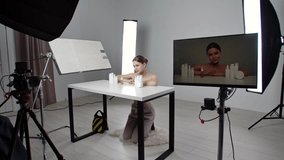 Backstage of professional cosmetic video shoot in studio. A young girl demonstrates jars with care cosmetics in a white studio. The cameraman turns on the camera, lighting equipment is visible. - Powered by Shutterstock - Get 15% off with code: PIKWIZARD15