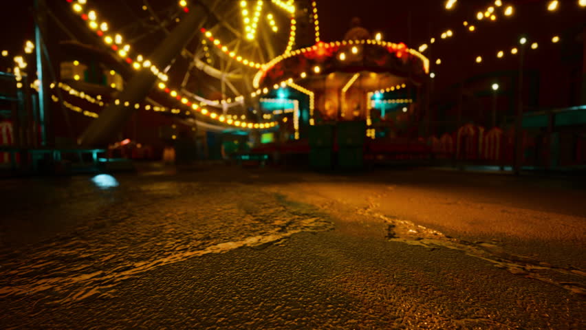 The amusement park stands deserted at night, with glowing lights from rides illuminating the empty pathways and wet ground, creating an eerie yet captivating atmosphere of stillness.
