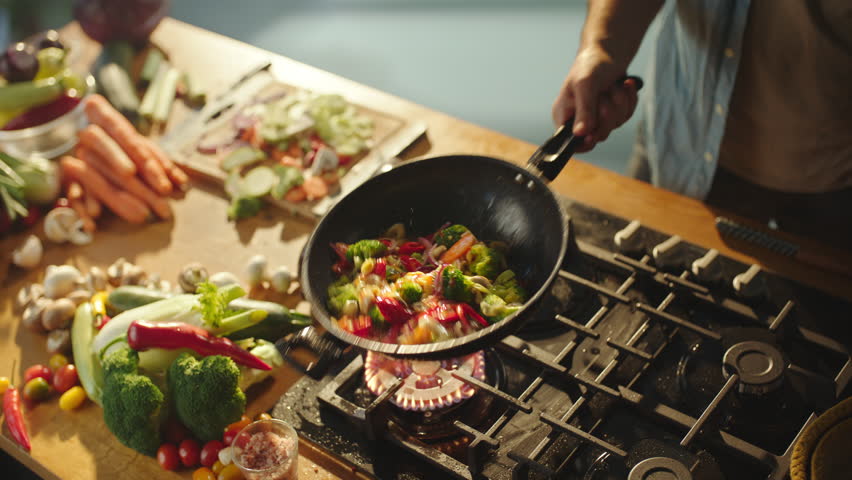 Close-up static shot of a chef tossing sliced vegetables in frying pan while cooking food in the kitchen