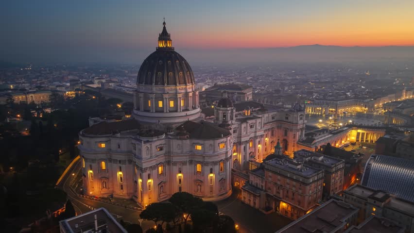 San Pietro Basilica at sunrise with city lights in Rome, Italy. Red sunrise sky at background. Aerial morning shot of St. Peter's Basilica in Vatican, Rome 