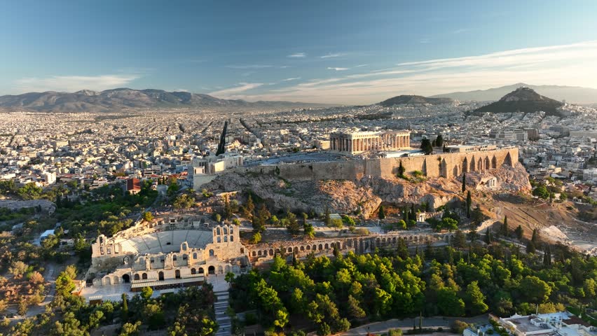 Fly around Parthenon in Athens - famous Greek tourist attraction. Aerial view of Parthenon in Athens, Greece at sunrise. Acropolis is illuminated with city lights, ancient theater sitting below