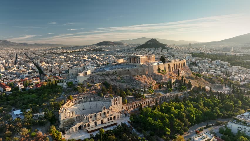 Fly around Parthenon in Athens - famous Greek tourist attraction. Aerial view of Parthenon in Athens, Greece at sunrise. Acropolis is illuminated with city lights, ancient theater sitting below