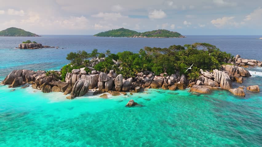 Aerial shot of small tropical island with palm trees and rocks in the Indian Ocean, Seychelles. Beautiful tropical island with turquoise waters and lush greenery surrounded by rocky formations