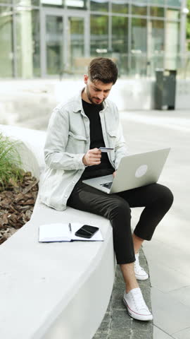Vertical Format Video of man customer using computer e-banking service making secure online payment holding credit card in hand. Male buyer paying on website via e commerce service near modern office.
