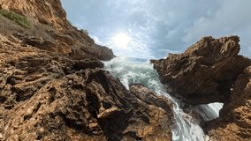 A powerful slow-motion capture of a wave bursting into foam, with sunlight filtering through droplets and splashes as the forceful water collides with jagged cliffs - Powered by Shutterstock - Get 15% off with code: PIKWIZARD15
