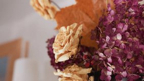 Close up of beige dried roses and purple hydrangeas with autumn leaves and red berries in rustic vase, creating warm natural decor in cozy indoor setting with blurred paper towel roll in background - Powered by Shutterstock - Get 15% off with code: PIKWIZARD15