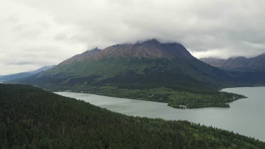 Huge mountain covered in clouds near lake and woodland, aerial view