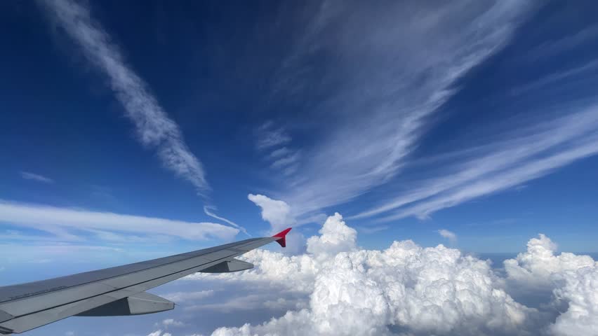 A breathtaking aerial view beautifully displaying an airplane wing gliding above fluffy clouds and vivid blue skies. Stunning Aerial View of Fluffy Clouds and an Airplane Wing Captured During Flight