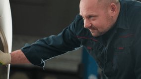 Mechanic in blue uniform using torchlight to inspect car tire in auto repair shop, focusing closely with blue lift in background, ensuring safety and maintenance in professional automotive workshop - Powered by Shutterstock - Get 15% off with code: PIKWIZARD15