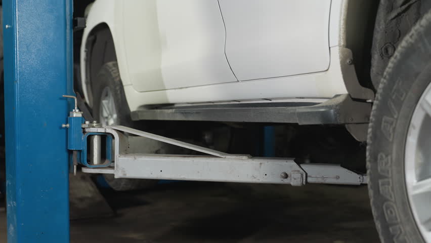 Detailed close-up of a white SUV being securely lowered from a hydraulic lift in an auto repair shop, focusing on the vehicle's side and lift mechanism