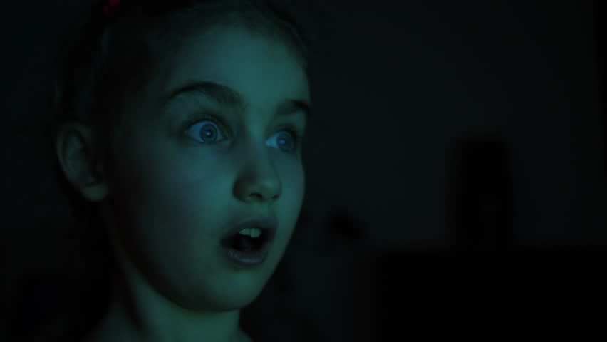 Portrait Child While Watching TV. Scared Girl Watch Television in Living Room. Addiction Video Game Entertainment. Little Scared Children Watching Horror Film or Video on TV or Computer in Dark Room.