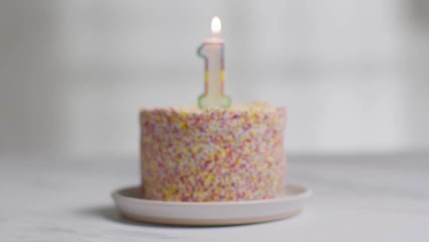 studio shot birthday cake covered with decorations and lit candle celebrating first birthday being blown out stock video