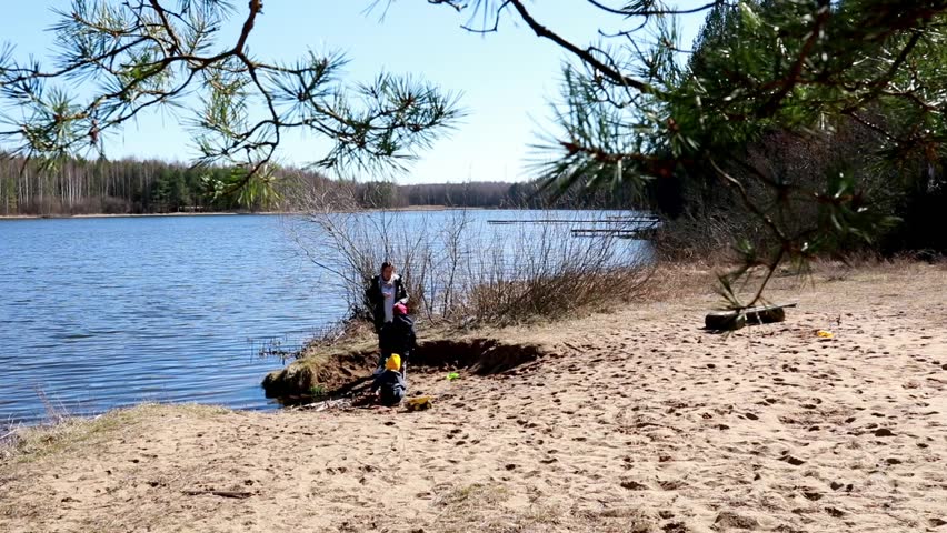 Children play by the water on a sunny day at the lakeside with sandy beach and lush scenery