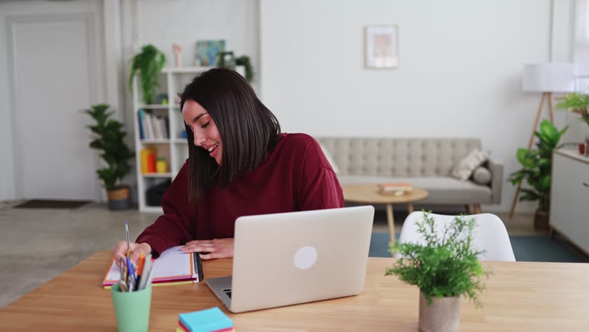 Young woman working from home on laptop and taking notes