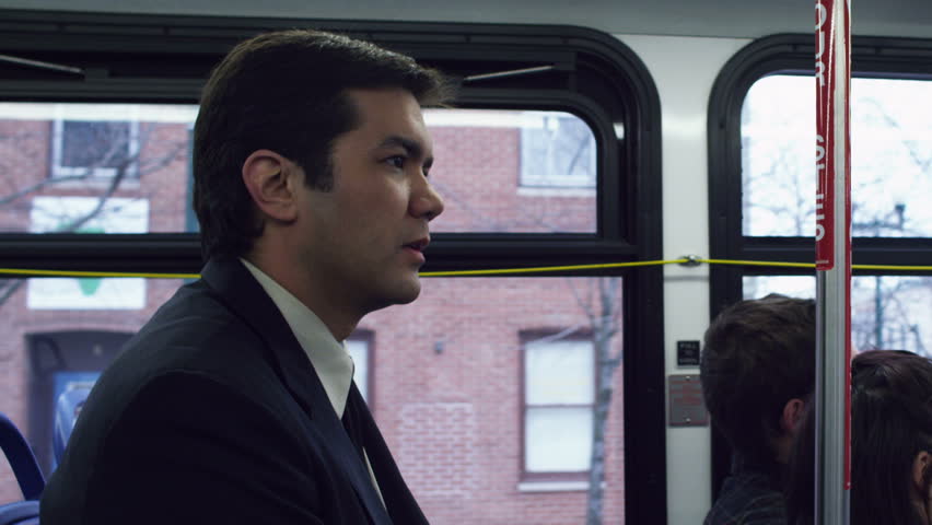 Man in a suit, riding the bus through a town or city. Mid shot.