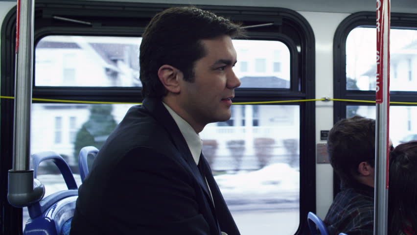 Man in a suit, riding the bus through a suburb. Mid shot.
