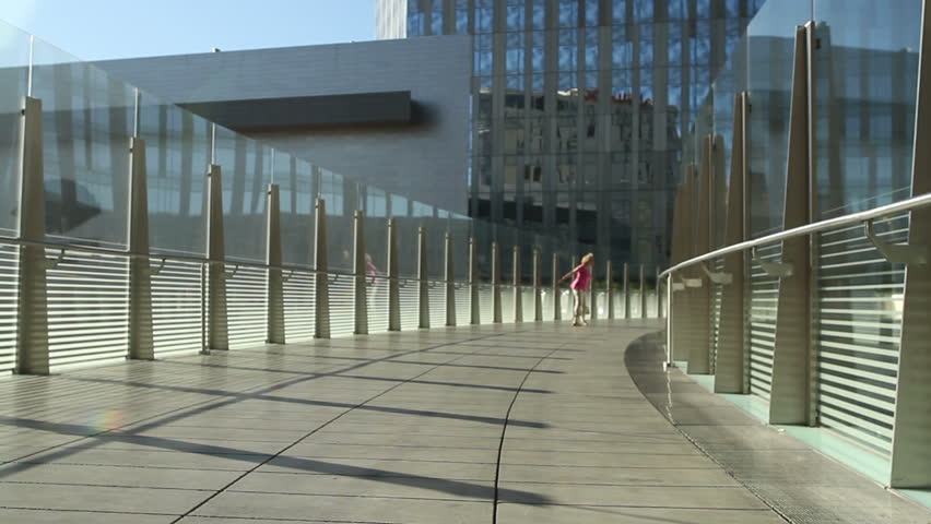 Woman crosses a modern pedestrian bridge, making some happy spins as she goes.