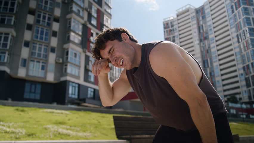 Tired Caucasian European young man sportsman running jogging morning training workout cardio exhausted guy male hard breathing stopping rest relaxing pause city outdoor sport healthy lifestyle runner