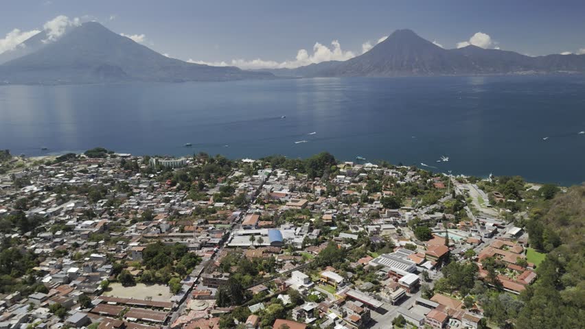 Drone flies backwards high above Panajachel, Guatemala with Lake Atitlan and two volcanoes on the skyline
