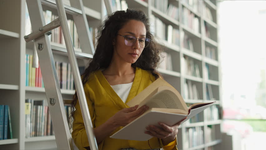 Latino Arabian woman librarian worker library ladder bookshelves textbooks knowledge education research turning pages holding book girl read bookworm reader teacher university learning study archive