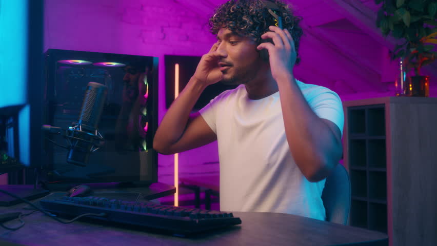 Latino Muslim Arabian man streamer blogger influencer puts on headphones microphone computer radio presenter host gamer stream male come sit guy online live broadcast talking player studio podcast web