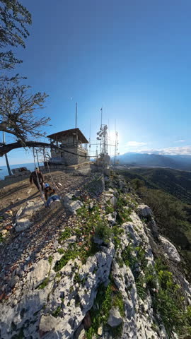 Vertical video. Man Pushing Woman on a Swing at the Edge of a Cliff on a Mountain Summit During a Romantic Evening with a Scenic View of the Valley and Mountains Under the Setting Sun