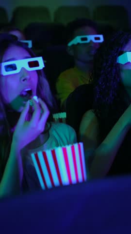 Young woman enjoying popcorn while watching a 3d movie in a cinema, surrounded by other spectators
