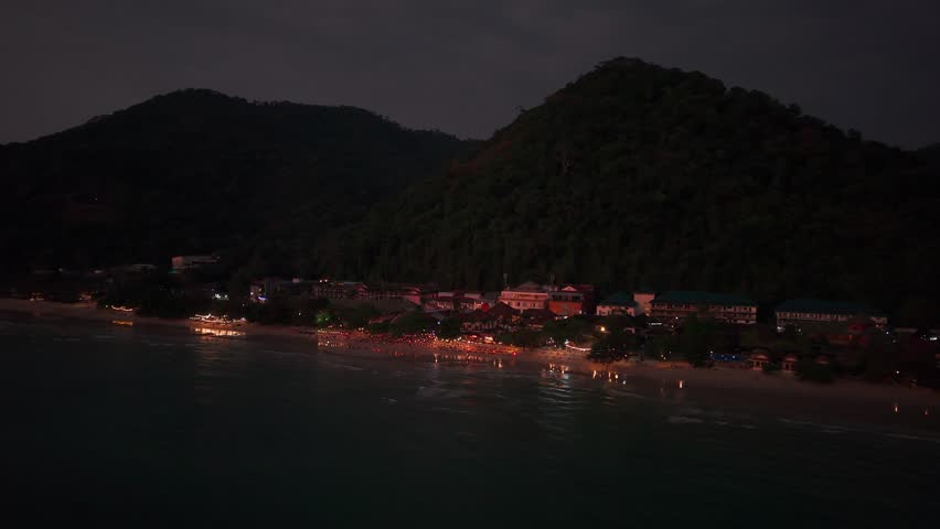 Warm party lights illuminating nighttime ocean waters along tropical coastline, casting vibrant reflections across serene koh chang island landscape during evening twilight