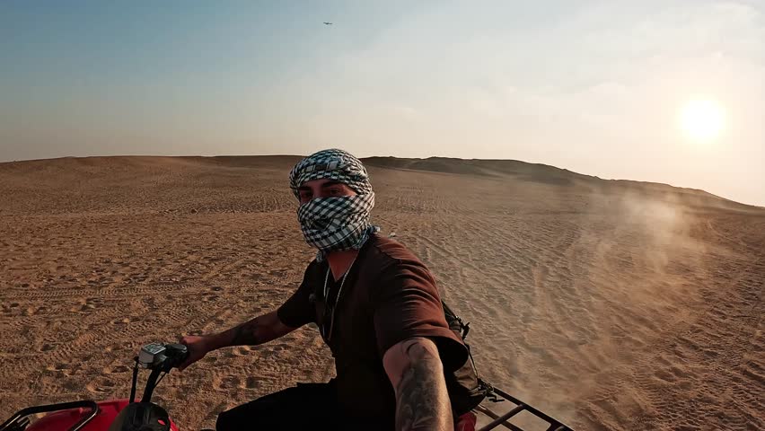 Tourist riding quad bike in desert at sunset