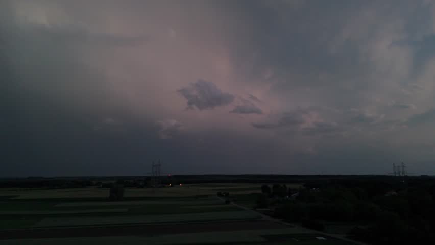 Aerial footage capturing a vivid lightning bolt cracking through dark storm clouds over flat fields at dusk.