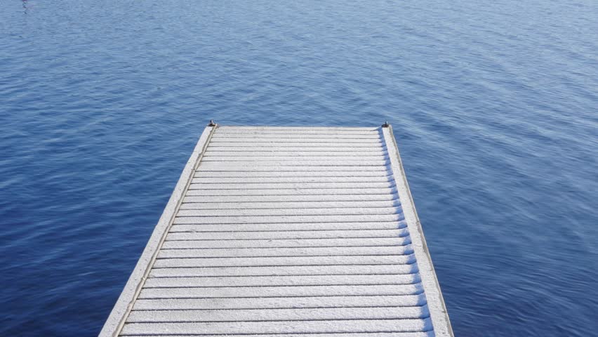 Snow covered pier or wooden dock blue eater moving in a tranquil winter setting. Slow motion 