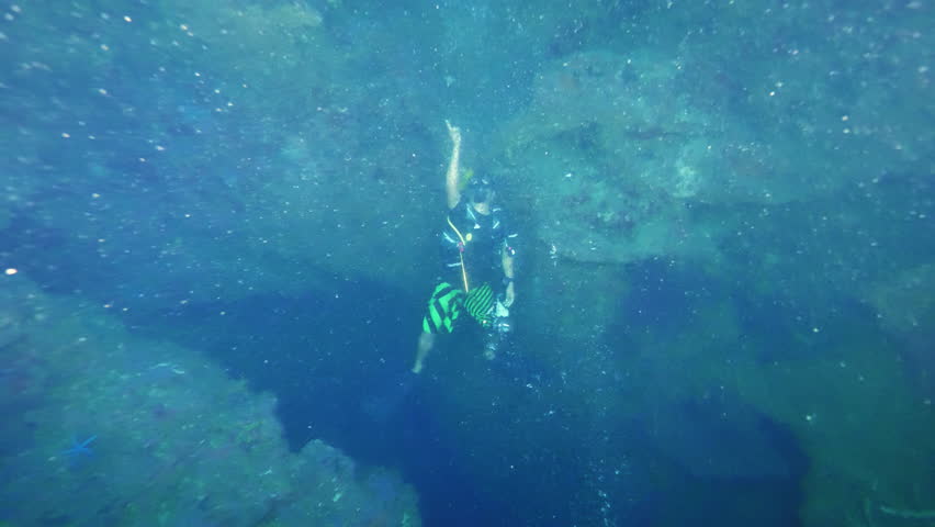 Diver traverses coral reef descending into oceans depths. Man signals gesticulating with hand to show marine environment to teammates in Philippines