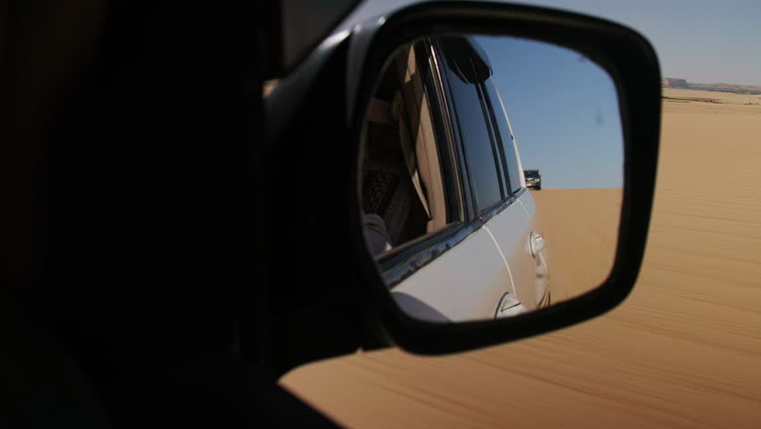 Offroad desert safari. SUV cars speeding in a sand dunes in Sahara desert. Reflection in rear view mirror. Handheld non-stabilized real-time footage