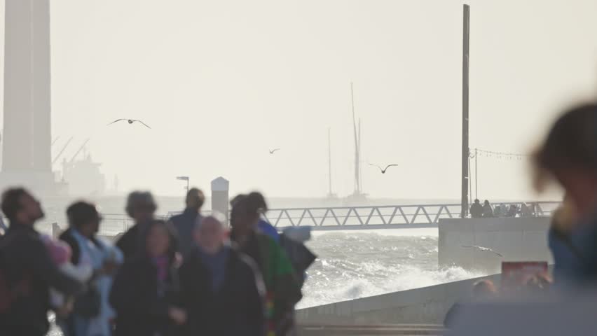 Tourists walking on pier, sailboat and seagulls flying in background