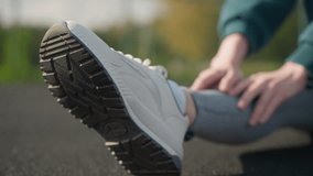 Close-up of person stretching outdoors, hands touching sneaker sole, showing fitness focus with well-manicured nails and textured athletic shoe, blurred background emphasizes flexibility - Powered by Shutterstock - Get 15% off with code: PIKWIZARD15