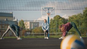Close-up of volleyball on the ground with blurred background featuring athletes stretching and exercising outdoors, a building can be seen in the distance under a clear sky - Powered by Shutterstock - Get 15% off with code: PIKWIZARD15