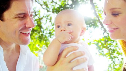 Smiling blonde baby girl close up held in loving parents arms in sunshine at park sun lens flare shot on RED EPIC