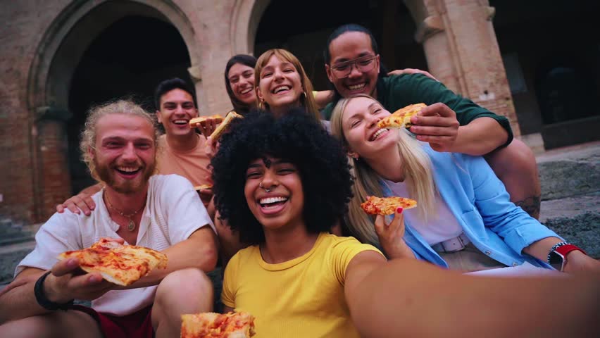 Funny selfie of a group of young people eating pizza in the touristic city. Italian friends having food outdoors, laughing in a casual street setting. Vibrant urban background and cheerful mood