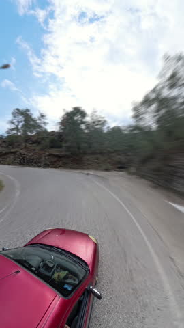 Vertical video. Time laps Red Car Moving on a Curved Mountain Road With Motion Blur Emphasizing Speed and Scenic Surroundings
