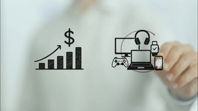 Businessman drawing an increasing profit graphic next to consumer electronics like headphones, smartwatch, laptop, game controller and desktop computer, circling them on a transparent board - Powered by Shutterstock - Get 15% off with code: PIKWIZARD15